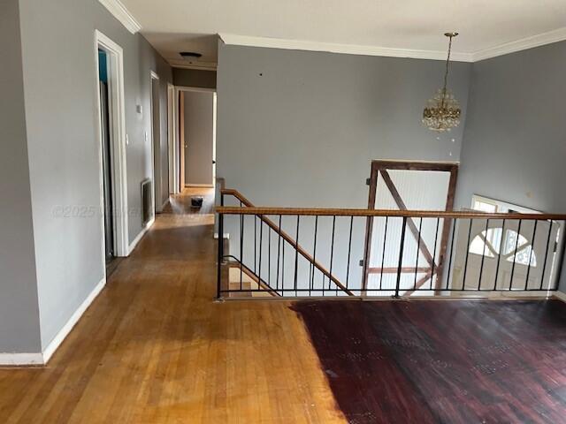 corridor featuring wood finished floors, an upstairs landing, ornamental molding, and a chandelier
