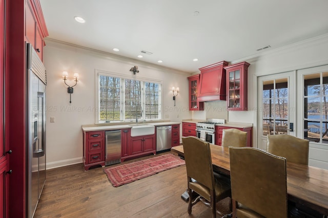 kitchen with a sink, visible vents, high end appliances, custom range hood, and red cabinets