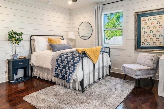 bedroom with dark hardwood / wood-style flooring and wooden walls