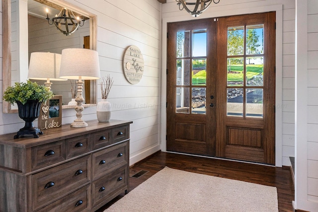 foyer featuring a chandelier, french doors, dark wood-type flooring, and wooden walls