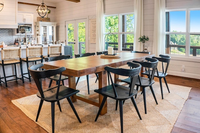 dining space featuring a notable chandelier, dark hardwood / wood-style floors, wood walls, and french doors