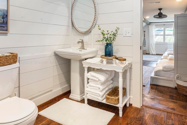 bathroom with wood-type flooring, toilet, and wood walls