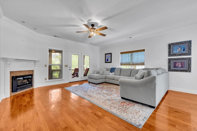 living room with a ceiling fan, ornamental molding, light wood finished floors, and a tile fireplace