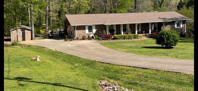 ranch-style home with a shed, a front lawn, driveway, an outbuilding, and a porch