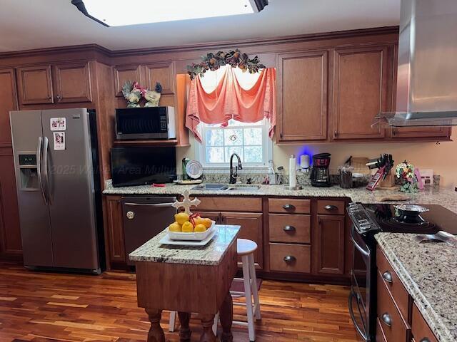 kitchen with stainless steel appliances, a sink, wood finished floors, brown cabinets, and light stone counters