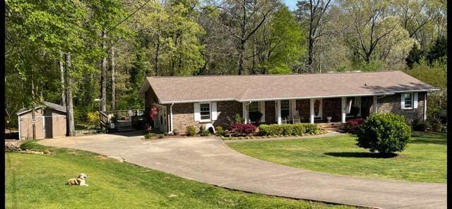 single story home with a storage shed, concrete driveway, an outdoor structure, a porch, and a front yard