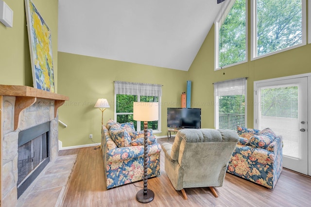living area with high vaulted ceiling, a fireplace with raised hearth, baseboards, and wood finished floors