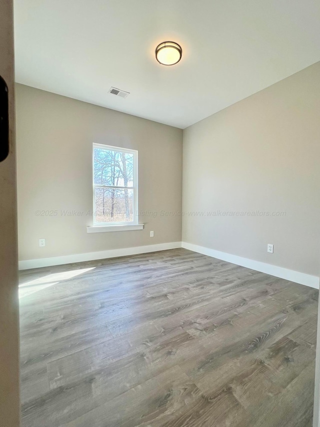 spare room with visible vents, baseboards, and wood finished floors