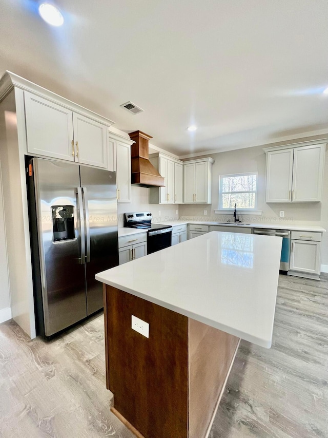 kitchen featuring visible vents, a kitchen island, light countertops, stainless steel appliances, and a sink