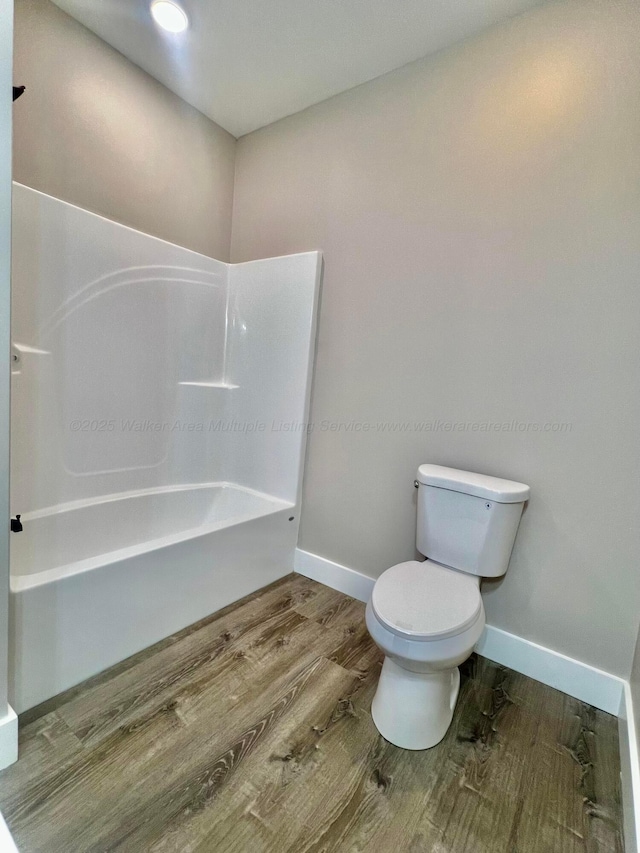 bathroom featuring bathtub / shower combination, toilet, wood finished floors, and baseboards