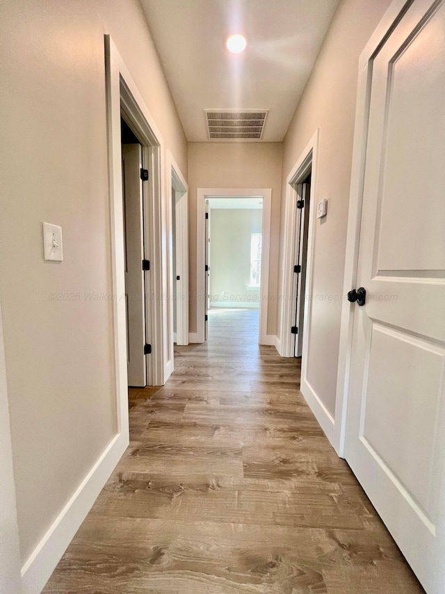 hall with visible vents, baseboards, and wood finished floors