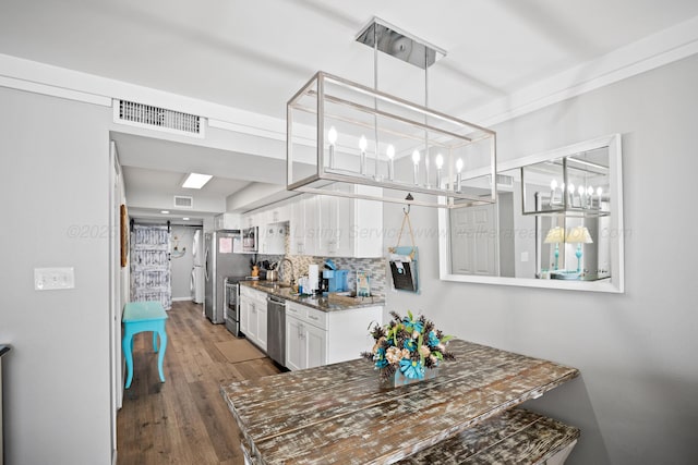 kitchen featuring a chandelier, white cabinets, a sink, stainless steel appliances, and backsplash
