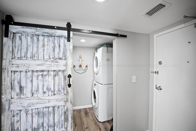laundry area with stacked washer and clothes dryer, a barn door, wood finished floors, and baseboards