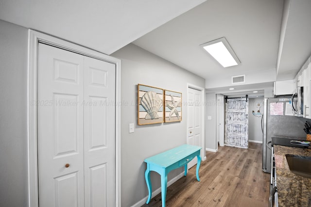 kitchen featuring stainless steel microwave, white cabinetry, light wood-style flooring, baseboards, and a barn door