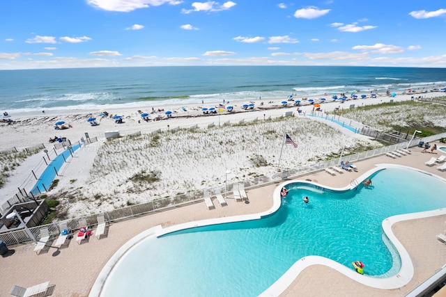 community pool with view of water and beach, fence, and a patio area