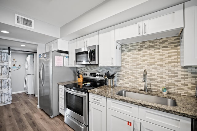 kitchen with appliances with stainless steel finishes, a sink, estacked washer and dryer, white cabinets, and backsplash