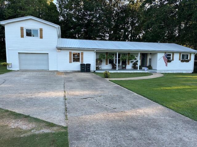 view of front of property featuring covered porch, a garage, and a front lawn