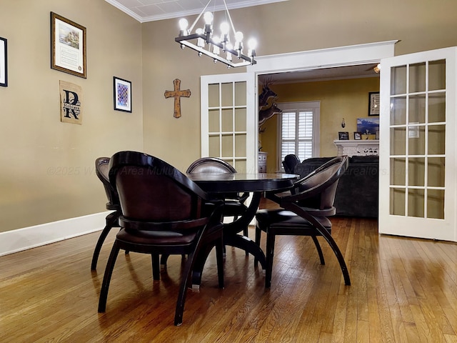 dining area with hardwood / wood-style floors, ornamental molding, baseboards, a chandelier, and a fireplace