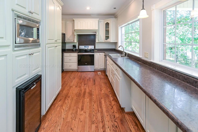 kitchen with dark countertops, appliances with stainless steel finishes, a sink, beverage cooler, and hanging light fixtures