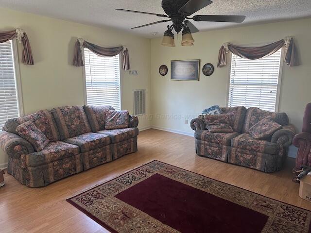 living area featuring a textured ceiling, visible vents, baseboards, wood finished floors, and a ceiling fan
