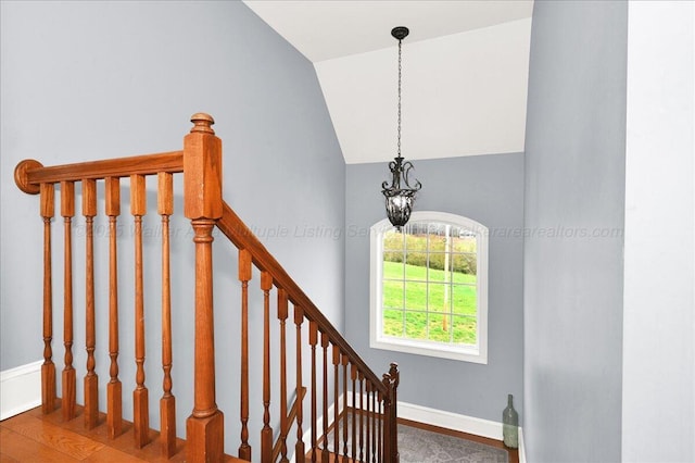 stairway with a notable chandelier, baseboards, vaulted ceiling, and wood finished floors