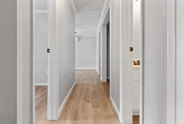 hallway featuring crown molding, baseboards, and light wood finished floors