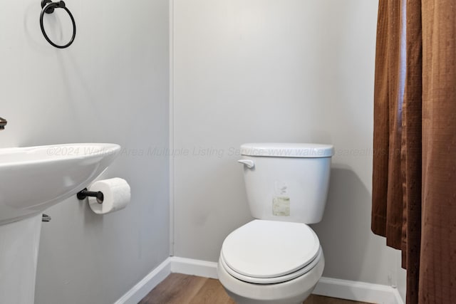 half bath featuring baseboards, wood finished floors, and toilet