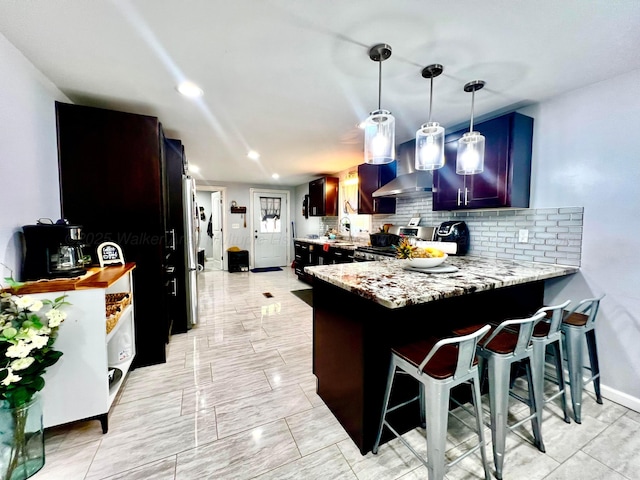 kitchen with a breakfast bar, gas stove, a peninsula, wall chimney exhaust hood, and tasteful backsplash