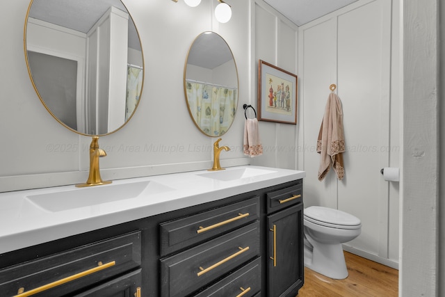 full bath featuring wood finished floors, double vanity, and toilet