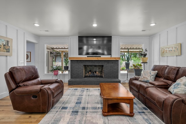 living room with wood finished floors, a decorative wall, a fireplace, and recessed lighting