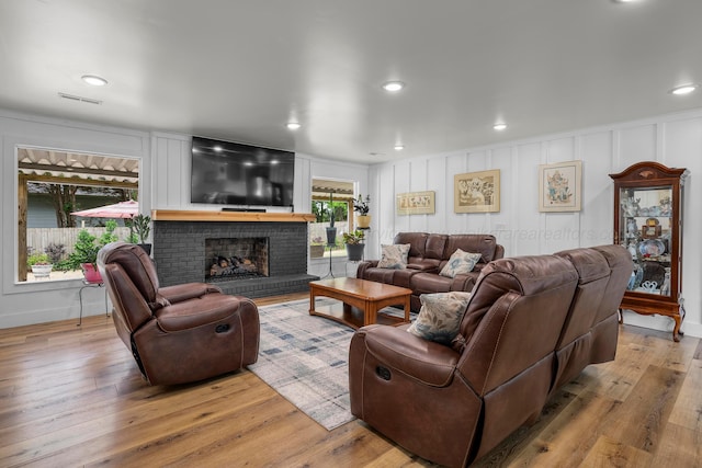 living area featuring a brick fireplace, light wood-style floors, recessed lighting, and a decorative wall