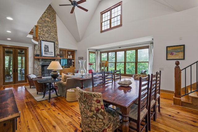 dining area featuring ceiling fan, wood-type flooring, a fireplace, and high vaulted ceiling