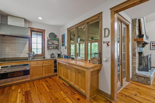 kitchen with light hardwood / wood-style floors, tasteful backsplash, wall chimney exhaust hood, and stainless steel oven