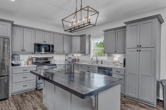 kitchen featuring dark wood-style floors, stainless steel appliances, gray cabinets, a sink, and a kitchen island