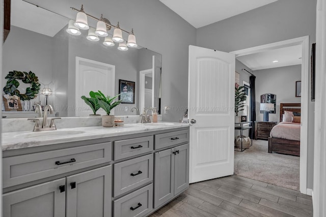 bathroom featuring wood finished floors, a sink, double vanity, and ensuite bathroom