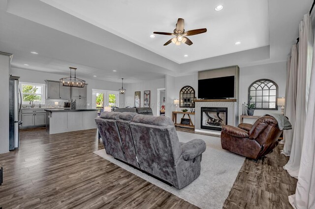 living room featuring a ceiling fan, a tray ceiling, a fireplace, dark wood-style flooring, and recessed lighting