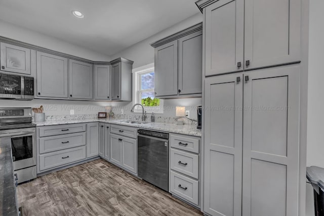 kitchen with light stone counters, a sink, gray cabinets, appliances with stainless steel finishes, and recessed lighting