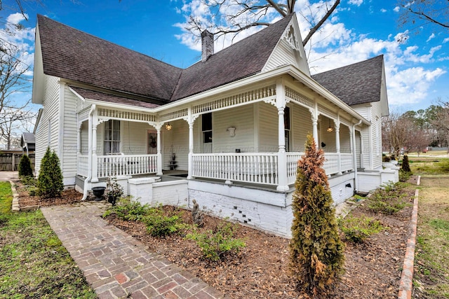 view of front of house featuring a chimney, a shingled roof, and a porch