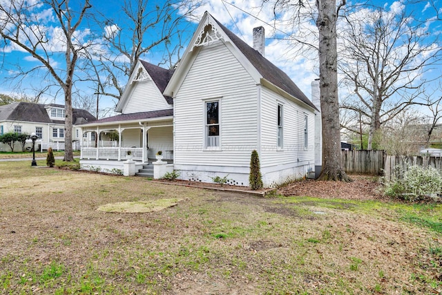 victorian house with a front yard, roof with shingles, a chimney, fence, and a porch