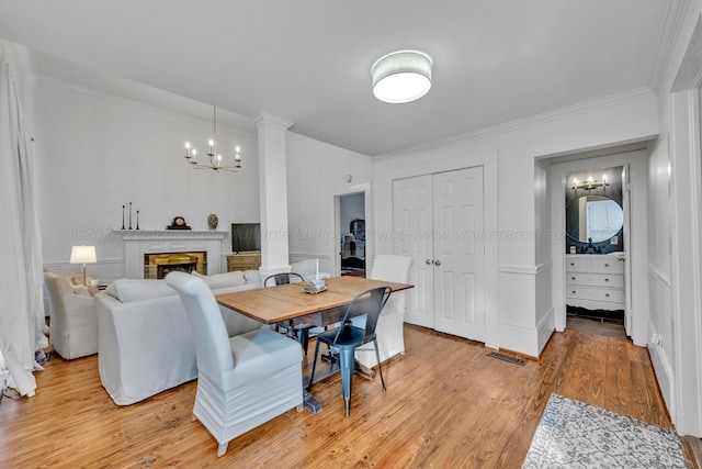 dining space featuring ornamental molding, a brick fireplace, a notable chandelier, and light wood finished floors
