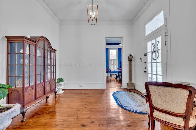 living area with baseboards, a notable chandelier, wood finished floors, and ornamental molding