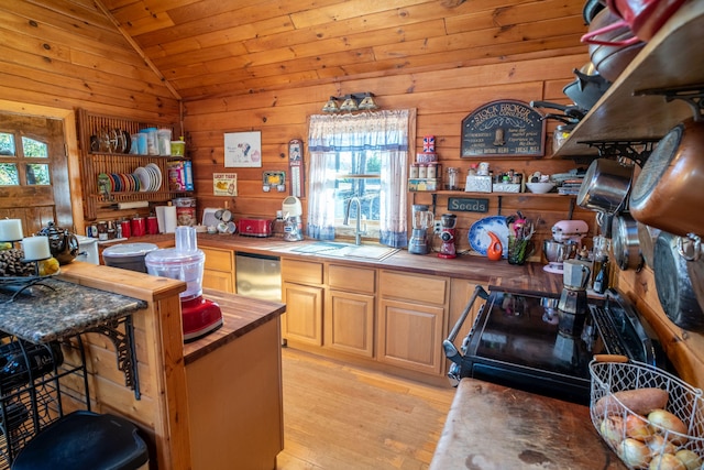 kitchen with wood walls, vaulted ceiling, stainless steel dishwasher, a sink, and light wood-style floors