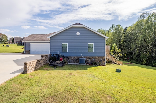 rear view of property featuring stairs, a garage, central AC, concrete driveway, and a yard
