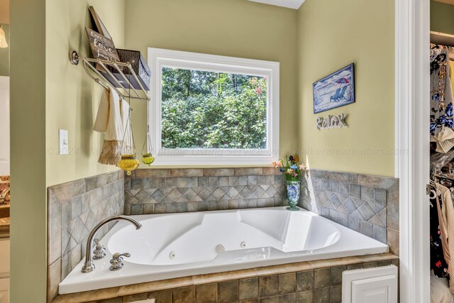 bathroom with a walk in closet and a tub with jets