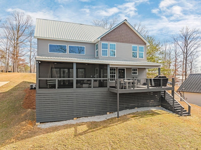 back of property with a sunroom, metal roof, stairs, a deck, and a lawn