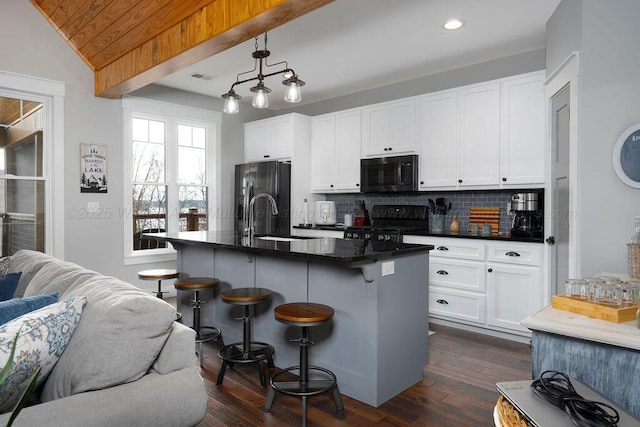 kitchen with decorative light fixtures, an island with sink, sink, a kitchen bar, and black appliances