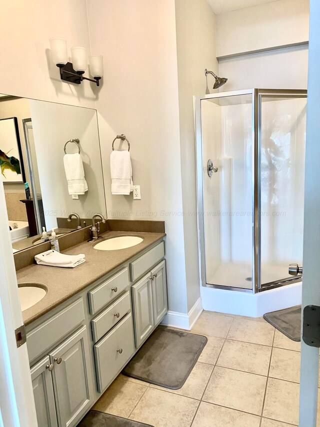 bathroom featuring tile patterned floors, a sink, a shower stall, and double vanity