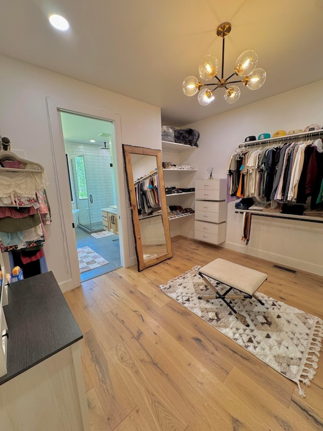 walk in closet featuring light wood-type flooring, visible vents, and an inviting chandelier