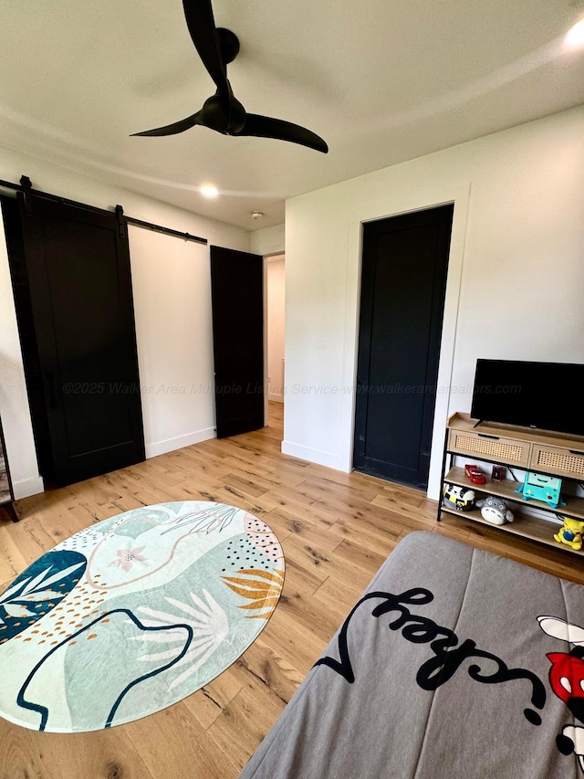 bedroom featuring a barn door, wood finished floors, a ceiling fan, and baseboards