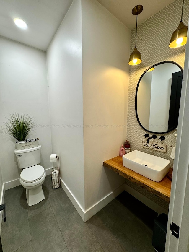 bathroom with wallpapered walls, baseboards, a sink, and toilet